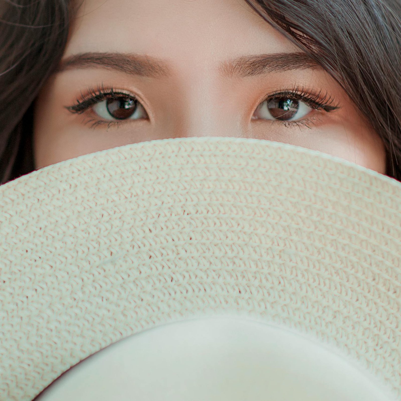 A captivating close-up of a woman's eyes above a stylish straw hat.